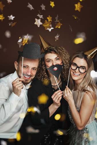 Group of happy people wearing party hats and using funny photo booth props are celebrating a holiday or event.