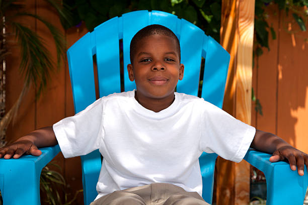 Eleven year old boy from the Honduran island of Roatan is sitting outside in front of a window and white wall posing for the camera. He is overweight. Taken with Canon 5D Mark lll.