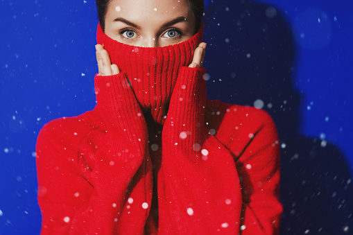 Surprised Woman in Red Turtleneck Bracing for Winter's Chill Against a Vivid Blue Backdrop.