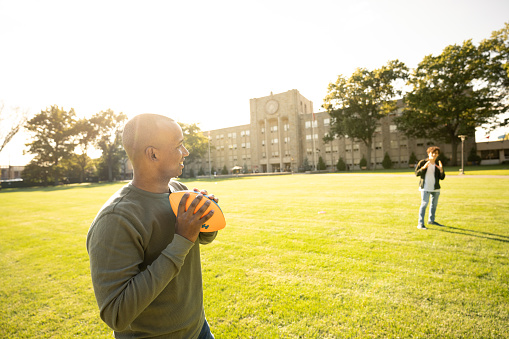 University students passing a football at sunset in a campus lawn at sunset