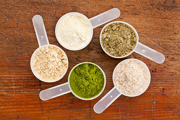 superfood supplement powder five plastic measuring cups of different superfood supplement powders (form bottom clockwise: wheatgrass, maca root, whey protein, hemp seed protein, psyllium husk) on grunge wood background protein drink stock pictures, royalty-free photos & images