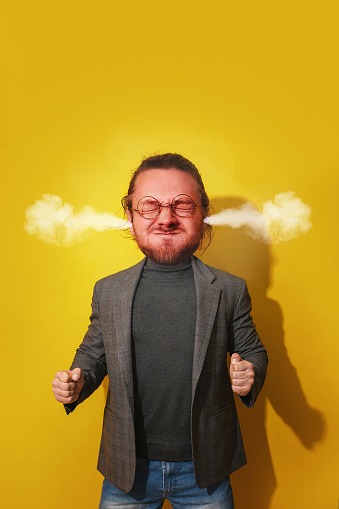 Irate man with an exaggeratedly large head, steam blowing from his ears against yellow background. Challenges of anger management.