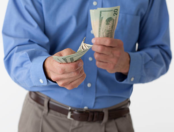 Man handing out cash Male in a blue dress shirt against a white background holds out $20 bills. uncle sam broke stock pictures, royalty-free photos & images