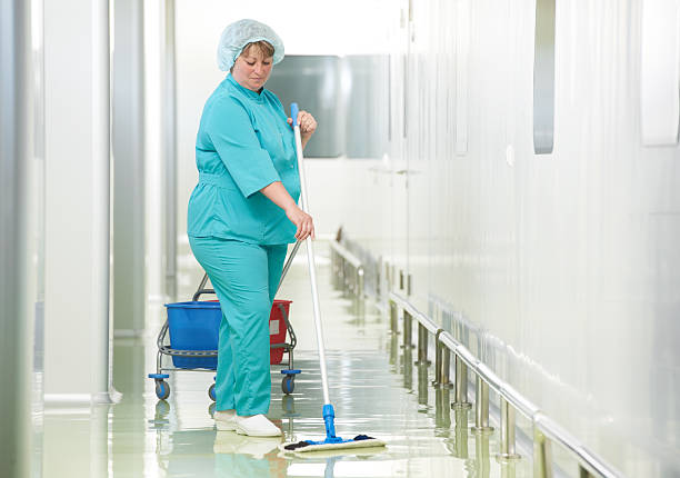 Adult cleaner maid woman with mop and uniform cleaning corridor pass floor of pharmacy industry factory or clinic