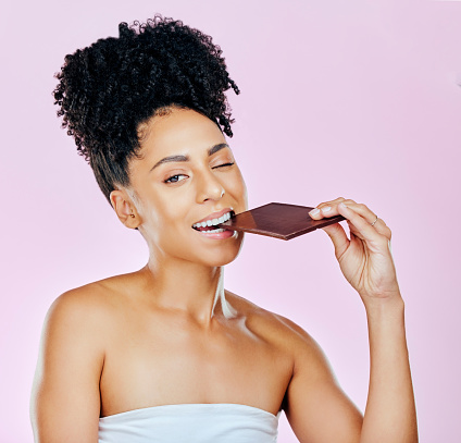 Portrait, sweet diet and woman with chocolate, eating and diabetes on a pink studio background. Face, person and model with unhealthy food, cacao treat and calories with sugar, nutrition and snack
