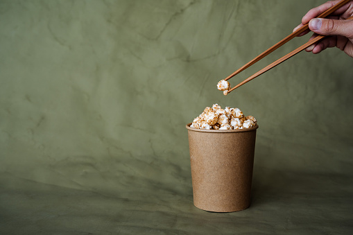 Chinese chopsticks to take popcorn from a box, a full can of popcorn, minimalistic style, on a colored background, concept picture, abstraction