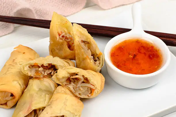 Close up of halved spring rolls served with chili sauce.