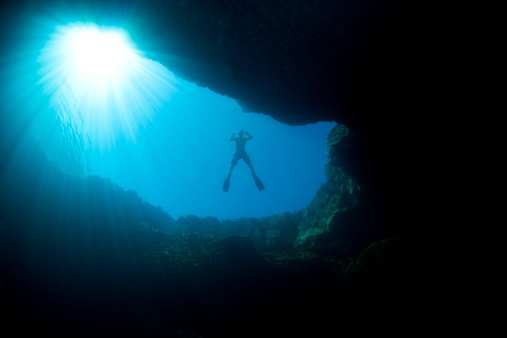 View towards the surface of a posing diver from an underwater cave