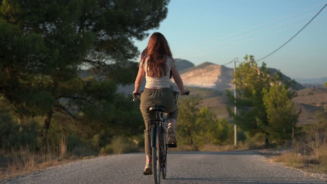 Young woman on a bicycle pedaling through the countryside at sunset