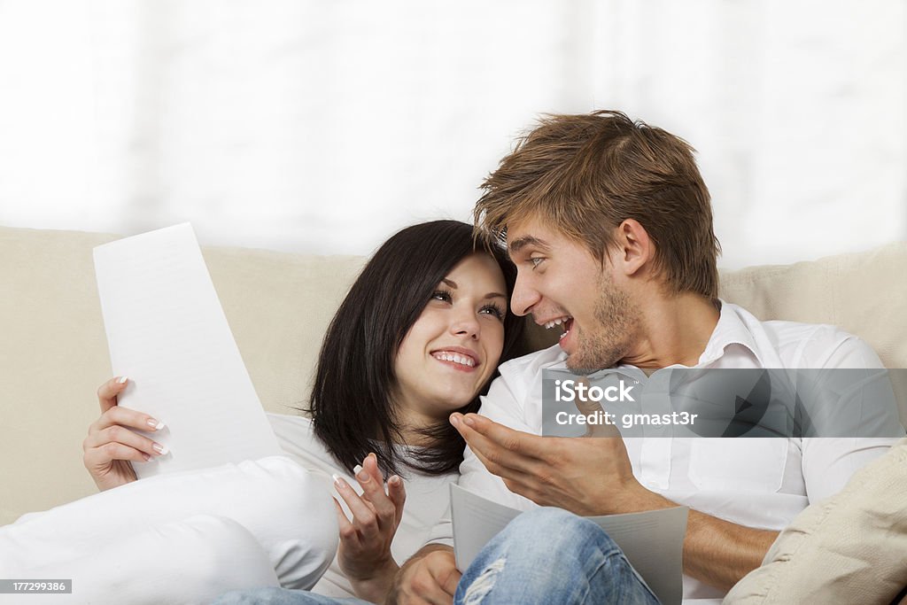 Couple sitting on couch at home "Happy couple reading a letter in their living room, young smile man and woman sitting on couch, sofa looking to each other talking" Mail Stock Photo