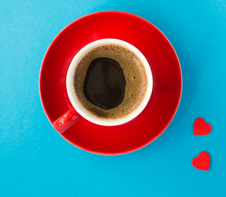 Coffee cup and two red hearts on the blue background. Close-up. Top view.