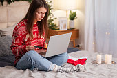 Christmas online shopping, sales and discounts promotions during winter holidays, online shopping at home. Female on bed with laptop with credit card and christmas decorations
