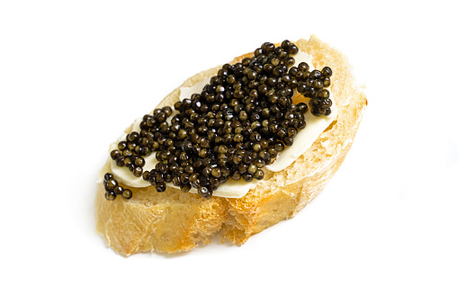 Baguette slice with black caviar and butter isolated over white. Natural sturgeon luxury delicacy sandwich closeup. Seafood delicatessen and bread appetizer.