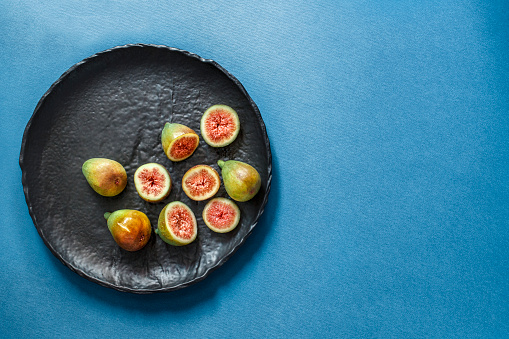 Still life with ripe sliced and whole fresh figs as healthy food for holidays. Blue background. Copy space. Flat lay. Overhead view.