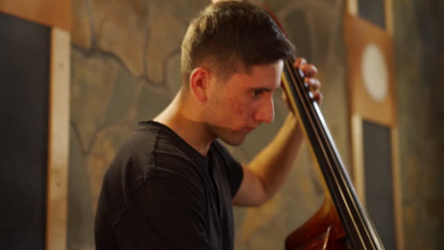 Young adult male student playing cello in music studio