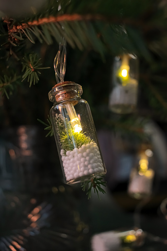 unusual creative Christmas lights on the Christmas tree, in the form of a glass bottle inside the fir tree and snow. Festive new year decor, dark composition, close up