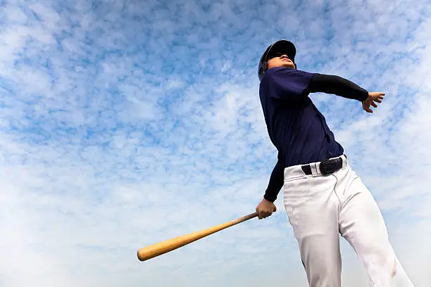 Photo of baseball player taking a swing with cloud background