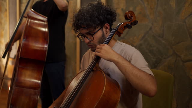 Adult Caucasian ethnicity playing cello in music recording studio