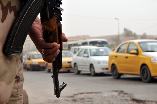 An Iraqi soldier armed with an assault rifle pointed to the ground watching traffic flow by at a roadblock in Baghdad. Narrow DOF, vehicles blurred.