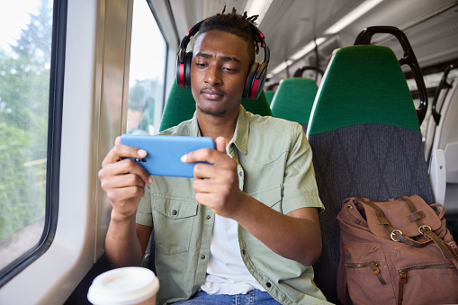 Young Man Commuting To Work Sitting  On Train Streaming And Watching Film Or Show On Mobile Phone