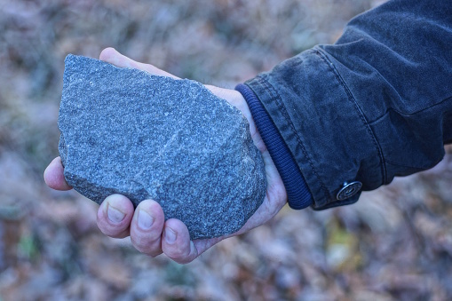 a one man hand holds a large gray piece of stone on a summer street