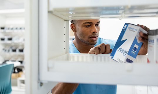 African American male nurse picking up some medicines at the hospital pharmacy - healthcare and medicine concepts