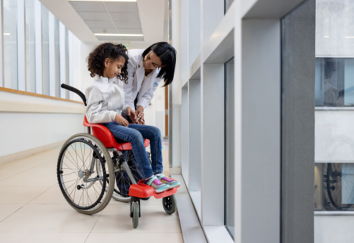 Latin American female doctor talking to a girl with cerebral palsy in a wheelchair at the hospital - healthcare and medicine concepts