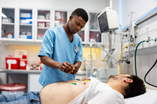 man arriving to the emergency room and nurse placing electrodes - borstelkegelden-fotos stockfoto's en -beelden