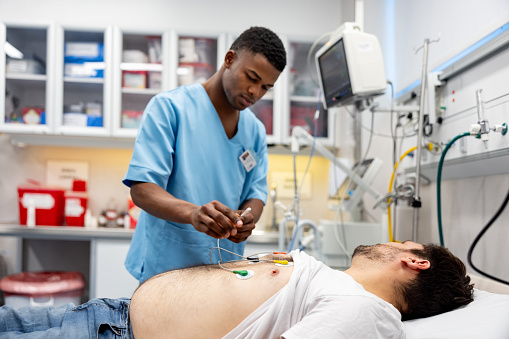 Man arriving to the emergency room and nurse placing electrodes on his chest - healthcare and medicine concepts
