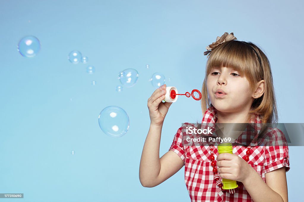 Girl blowing soap bubbles Portrait of little girl blowing soap bubbles over blue background Bubble Wand Stock Photo