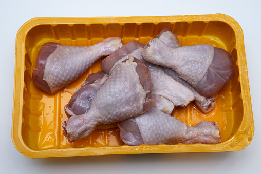 raw chicken legs in a plastic container on a white background