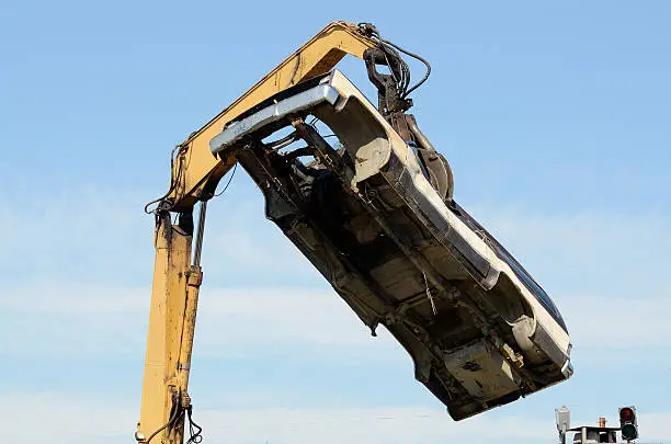 Large excavator with a claw crushing and piling old cars at a metal recycle plant