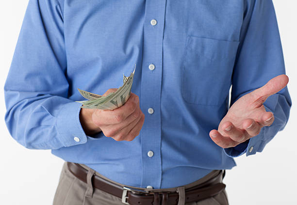 Man holding Cash Male in blue dress shirt against a white background holding American currency. His other hand suggests he is unsure and questioning the action. uncle sam broke stock pictures, royalty-free photos & images