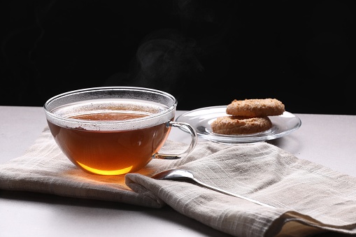 Glass cup of tea with cookies on table against black background