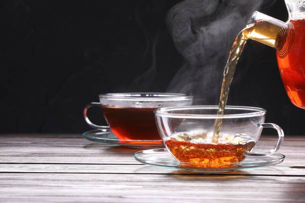 istock Pouring tea into glass cup on wooden table against black background, space for text 1773170782
