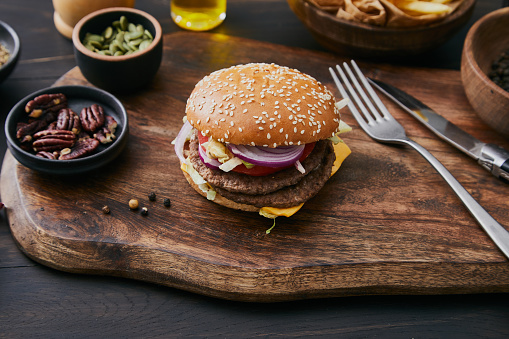 Fresh, tasty and delicious double beef cheeseburger with French fries, tomato, Spanish onion, served  on a plate, bar, restaurant or home kitchen table, close up view with copy space, representing fast food and city life, indulgence and joy through gourmet lifestyle