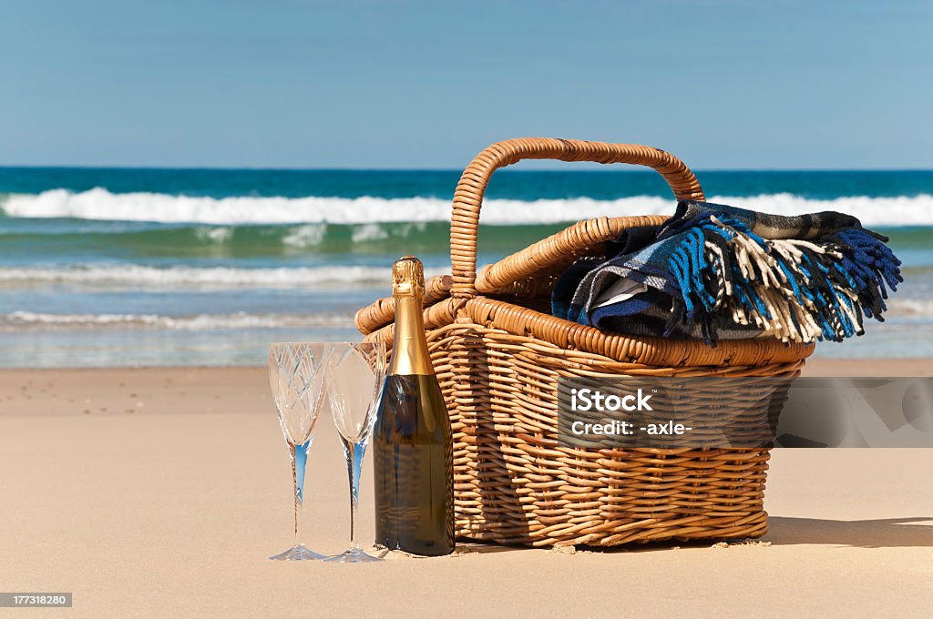 Basket ready for a beach picnic with two champagne glasses Champagne,glasses,picnic basket and blanket,perfect for a afternoon at the beach. Picnic Basket Stock Photo