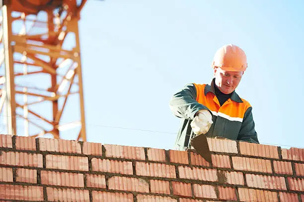 construction mason worker bricklayer installing red brick with trowel putty knife outdoors