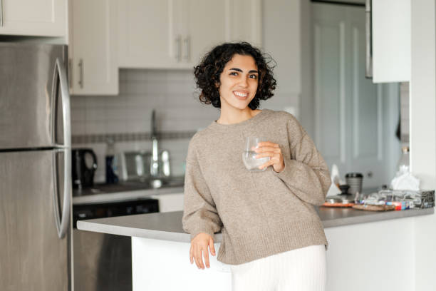istock Beautiful curly middle eastern woman looking at camera and drinking water at home 1773210671