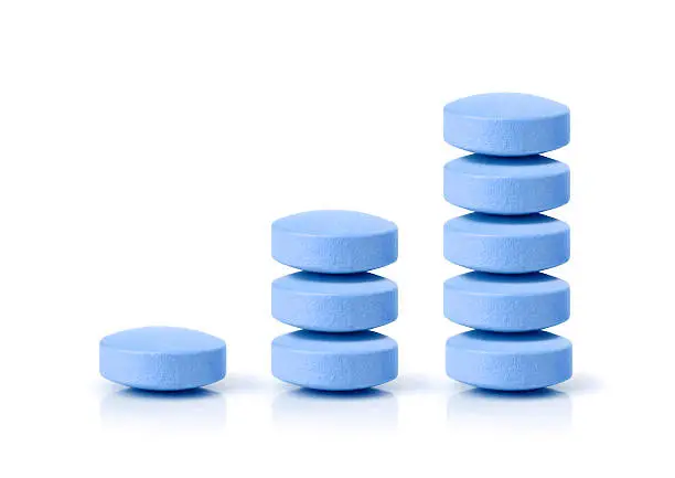 Growth graph made of stacked blue pills on white background with reflection. Concept: growing pharmacy market and increasing demand for blue pill and it's substitutes.