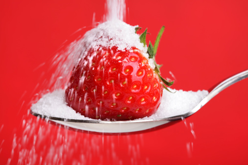 Pouring sugar over a strawberry on a spoon