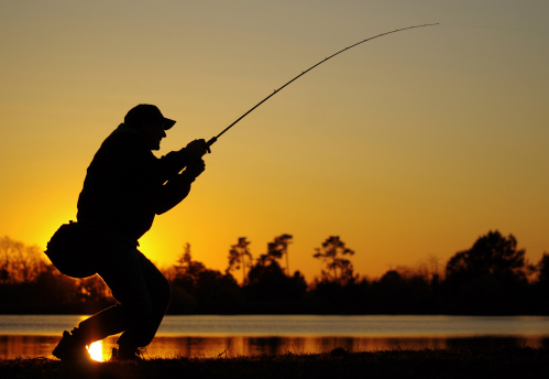 A fisherman fight against a bass at sunset