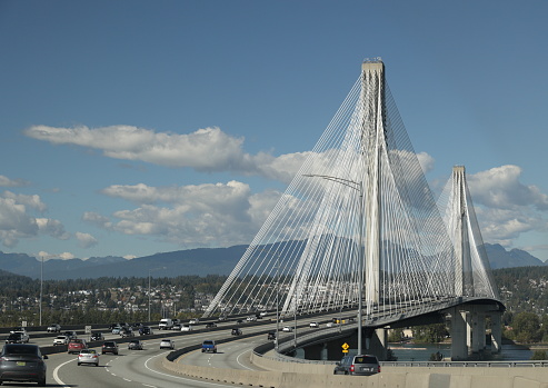 Surrey, Canada - September 30, 2023: Traffic heads north from Surrey to Coquiltam and Burnaby on the Trans-Canada Highway carried by the Port Mann Bridge. This cable-stayed bridge spans the Fraser River. Background shows clouds over the North Shore Mountains in autumn.