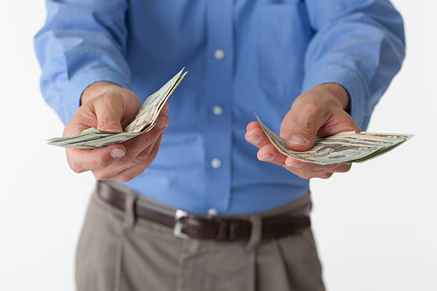 Man holding out cash Male wearing a blue dress shirt against a white background holds out $20 US bills with both hands. uncle sam broke stock pictures, royalty-free photos & images