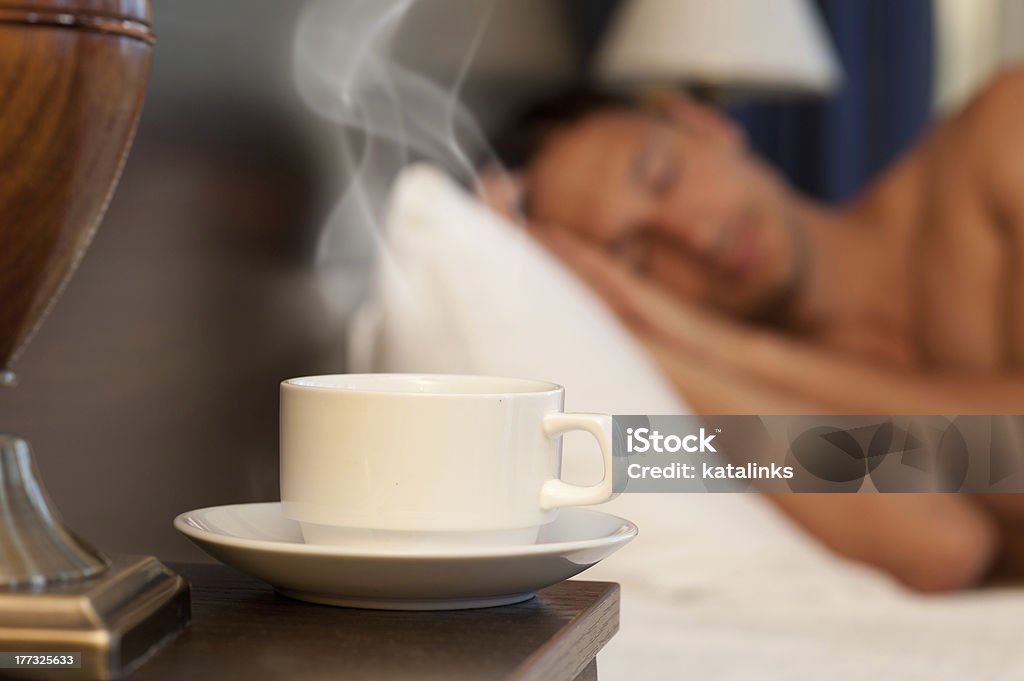man sleeping on abed, a cup of hot tea "man sleeping on a bed, a cup of hot steaming coffee on the bedside table and lamp" Adult Stock Photo