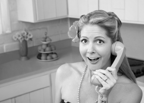 Happy retro-styled Caucasian woman on phone in kitchen