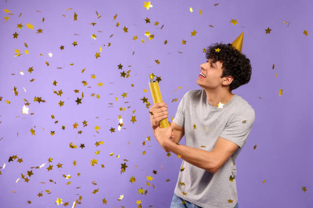 istock Handsome young man blowing up party popper on violet background 1773271178