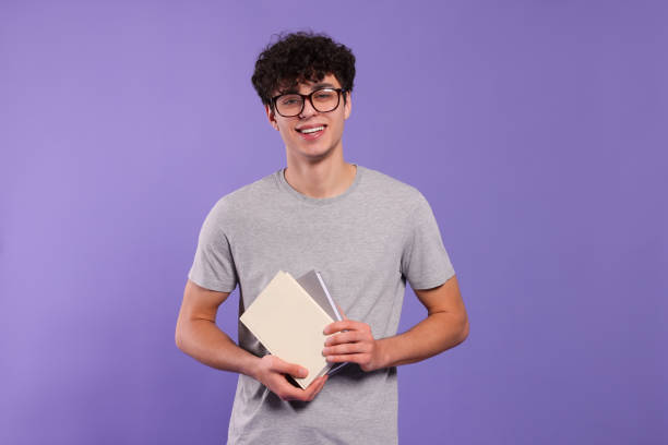 istock Handsome young man with books on violet background 1773272251