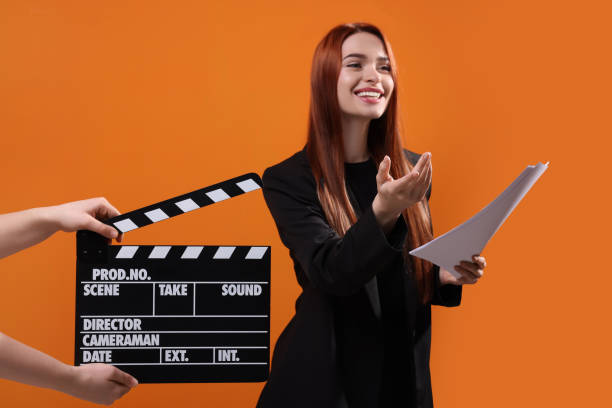 Actress performing role while second assistant camera holding clapperboard on orange background, selective focus Actress performing role while second assistant camera holding clapperboard on orange background, selective focus color image performing arts event performer stage theater stock pictures, royalty-free photos & images