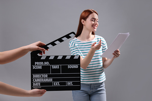 Actress performing role while second assistant camera holding clapperboard on grey background, selective focus
